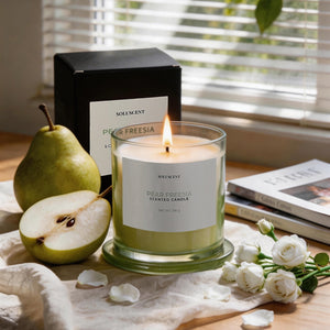 Pear Freesia candle lit beside its packaging box, with a pear and white roses